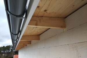 Building fasade under construction with unfinished wall and wooden roof boards with plastic gutter